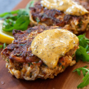Wooden cutting board with Lions Mane Crab Cakes topped with a sauce
